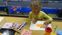 Участница конкурса рисования  акварельными красками старательно рисует рыбку.